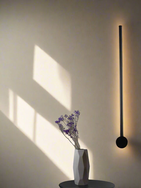 Tatva Lights minimalist vertical wall LED light in matte black finish – modern ambient wall lamp for living rooms, hallways, or contemporary interiors with indirect warm lighting.