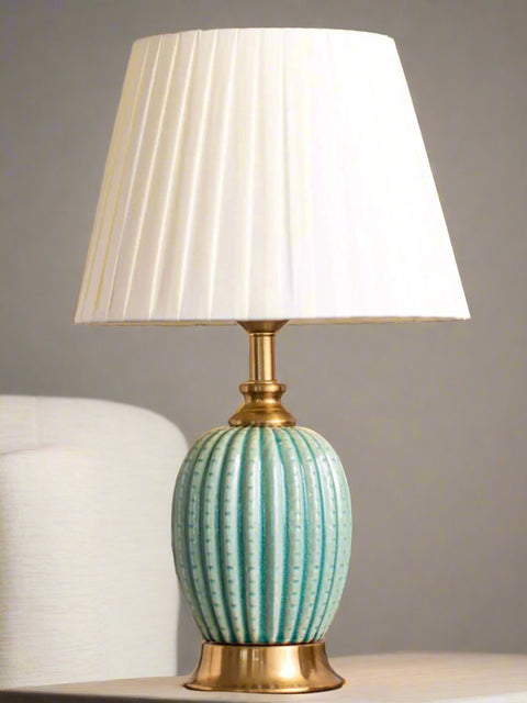 Tatva Lights Fluted Ceramic Table Lamp with a mint green, vertically ribbed base and gold accents, topped with a pleated white fabric lampshade—perfect for adding a refined touch to bedside tables or console setups.