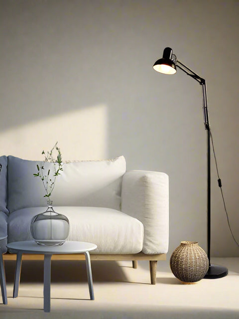 Tatva Lights Adjustable Swing Arm Floor Lamp โ A sleek black metal floor lamp with a dome-shaped shade and movable swing arm, placed beside a minimalist white sofa. Perfect for modern interiors, reading nooks, or ambient task lighting.