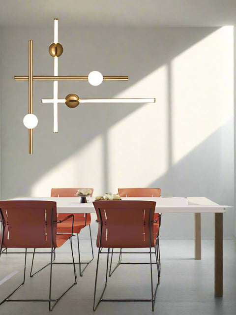 Modern gold chandelier with four lights hanging over a white kitchen counter, surrounded by orange wall panels and black chairs.