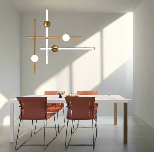 Modern gold chandelier with four lights hanging over a white kitchen counter, surrounded by orange wall panels and black chairs.