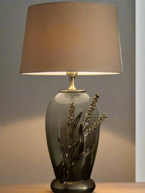 Tatva Lights Exquisite Handcrafted Table Lamp featuring a smoky glass base adorned with intricate metallic floral detailing and topped with a soft taupe fabric lampshade—an artfully crafted piece that brings warmth, elegance, and natural charm to any space.
