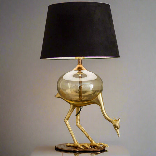 Tatva Lights Flamingo Metal Glass Table Lamp featuring a sculpted golden flamingo base, round glass body, and elegant black lampshade—perfect for adding a bold, artistic touch to luxury modern interiors.