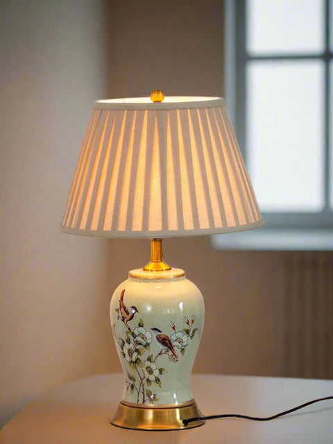 Tatva Lights Floral Ceramic Yellow and Green Table Lamp featuring a hand-painted floral and bird motif on a glazed ceramic base, complemented by a pleated fabric shade and golden accents for a classic and elegant look.