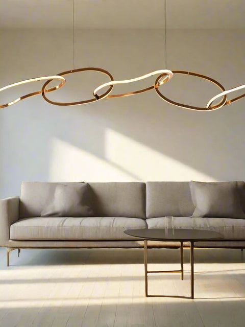 Tatva Lights Contemporary gold LED chandelier with flowing, interconnected oval loops and sculptural wave design, suspended from the ceiling. Statement pendant lighting ideal for modern living rooms, dining areas, or luxury interiors.