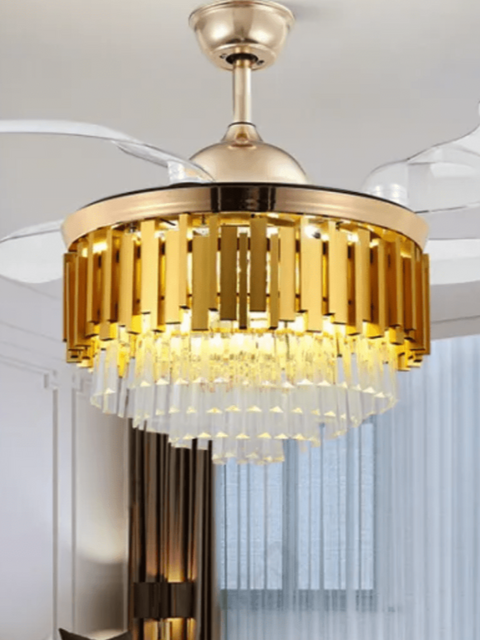 A luxurious golden crystal ceiling fan with an chandelier-style light fixture, featuring automatic retractable fan blades and a remote control, installed in a living room setting.