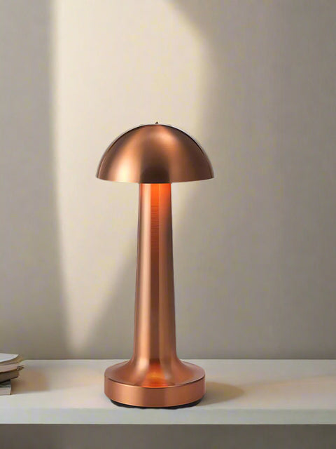 Tatva Lights Mushroom Touch-Control Wireless Bar Table Lamp in a sleek metallic copper finish, featuring a dome-shaped top and slender stem design. Placed on a marble surface against a dark backdrop, the lamp adds a warm, modern glow ideal for contemporary bar or side table settings.