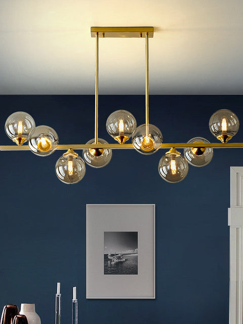 A luxurious raindrop-style chandelier with gold metal structure and clear glass globe bulbs, hanging in a room with a dark blue wall and a framed picture on the wall.