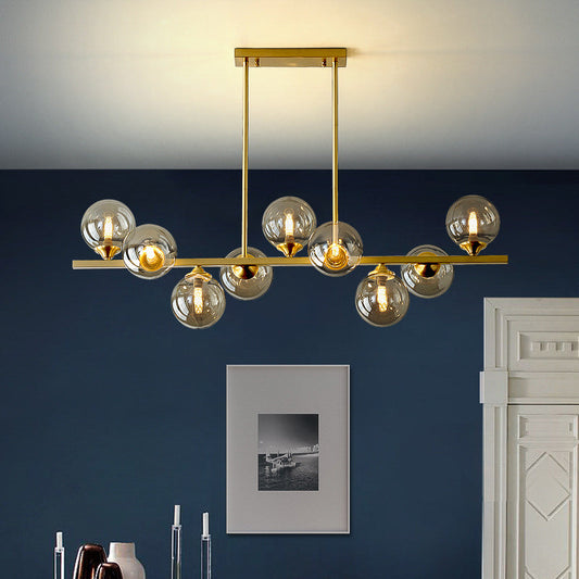 A luxurious raindrop-style chandelier with gold metal structure and clear glass globe bulbs, hanging in a room with a dark blue wall and a framed picture on the wall.