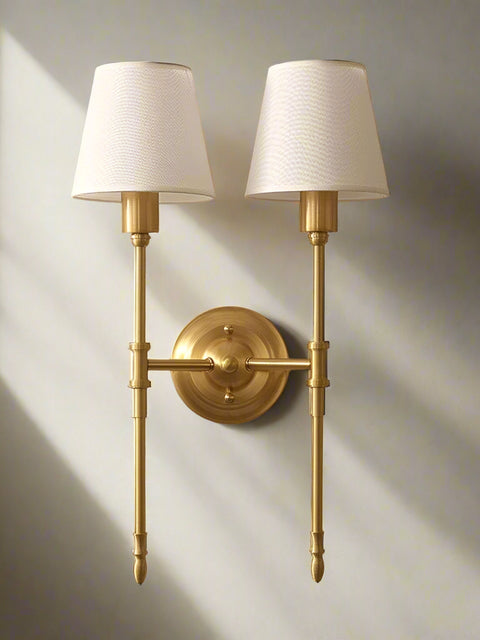 Tatva Lights NOVA IRON Wall Lamp – a timeless dual-arm wall sconce with a luxurious brushed gold iron frame and classic white fabric shades. This elegant lighting fixture adds a refined, vintage-inspired charm to living rooms, bedrooms, hallways, or upscale interiors, combining modern craftsmanship with traditional aesthetics for ambient and focused illumination.