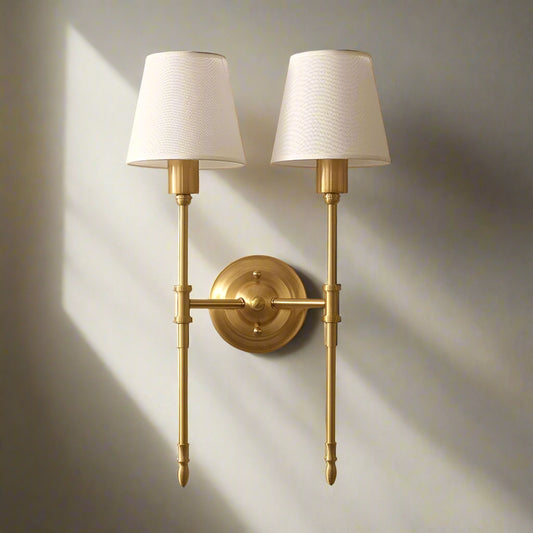 Tatva Lights NOVA IRON Wall Lamp – a timeless dual-arm wall sconce with a luxurious brushed gold iron frame and classic white fabric shades. This elegant lighting fixture adds a refined, vintage-inspired charm to living rooms, bedrooms, hallways, or upscale interiors, combining modern craftsmanship with traditional aesthetics for ambient and focused illumination.