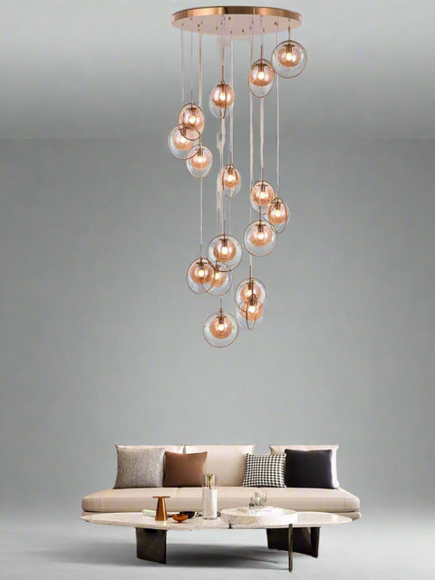 Tatva Lights Novaré Double Height Chandelier features a grand, multi-tiered design with cascading crystal elements and a warm gold finish, ideal for illuminating large foyers, staircases, or double-height living areas with timeless elegance.