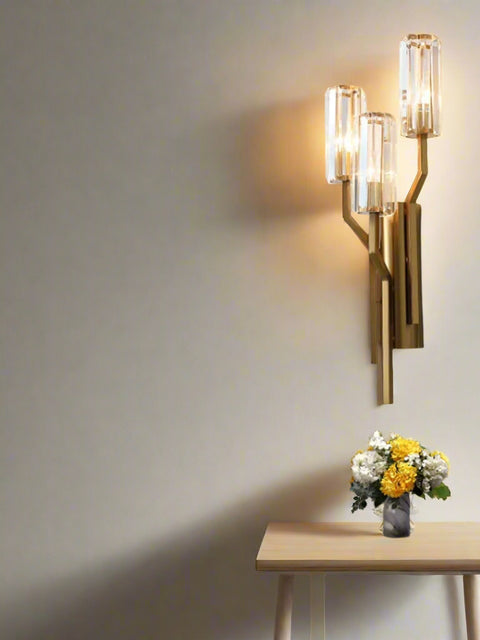 Tatva Lights Tribus Flambeau LED Wall Light featuring a luxurious gold metal frame with three crystal cylindrical diffusers, designed to resemble a branching structure. Perfect for adding elegance and ambient lighting to modern living spaces.