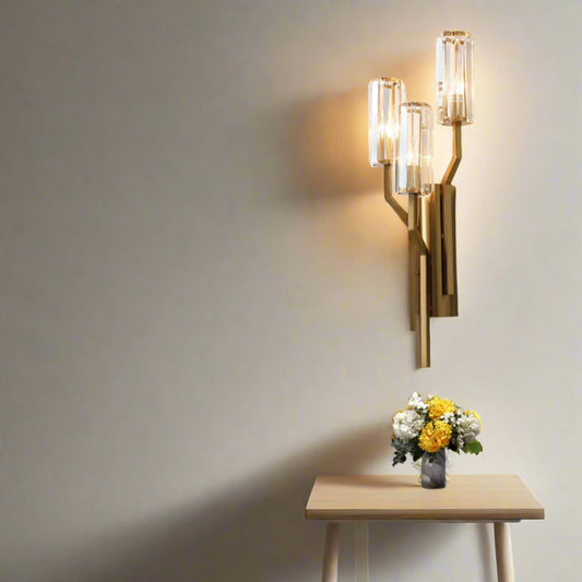 Tatva Lights Tribus Flambeau LED Wall Light featuring a luxurious gold metal frame with three crystal cylindrical diffusers, designed to resemble a branching structure. Perfect for adding elegance and ambient lighting to modern living spaces.