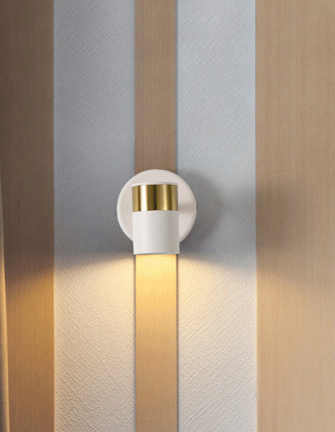 A white and gold LED ceiling wall light mounted on a wall, emitting a warm white glow, situated above a striped surface possibly indicating a home interior setting.