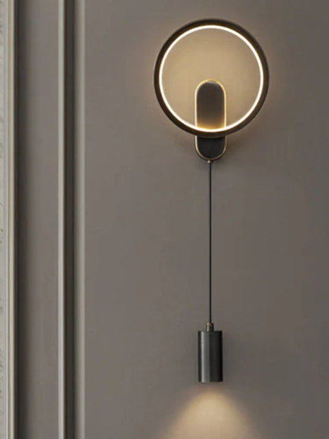 Modern LED wall light fixture with a circular design, mounted on a wall in a room with a marble wall and a fireplace.