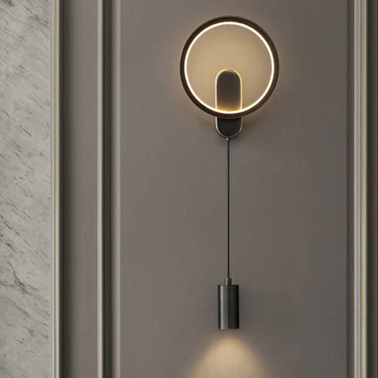 Modern LED wall light fixture with a circular design, mounted on a wall in a room with a marble wall and a fireplace.