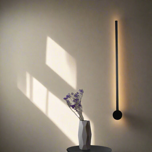 Tatva Lights minimalist vertical wall LED light in matte black finish – modern ambient wall lamp for living rooms, hallways, or contemporary interiors with indirect warm lighting.