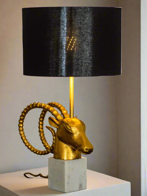 Tatva Lights Bighorn Bedside Table Lamp featuring a striking gold-finished bighorn sheep head with coiled horns, mounted on a white marble base and topped with a sleek black drum lampshade; a bold blend of luxury and artistry for modern interiors.
