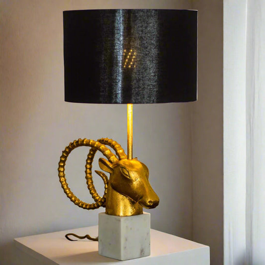 Tatva Lights Bighorn Bedside Table Lamp featuring a striking gold-finished bighorn sheep head with coiled horns, mounted on a white marble base and topped with a sleek black drum lampshade; a bold blend of luxury and artistry for modern interiors.