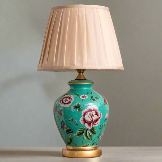 Tatva Lights Bloom Ceramic Table Lamp featuring a vibrant turquoise base adorned with hand-painted floral and butterfly motifs, complemented by gold accents and a pleated beige lampshade—an elegant fusion of color and charm for classic or eclectic interiors.