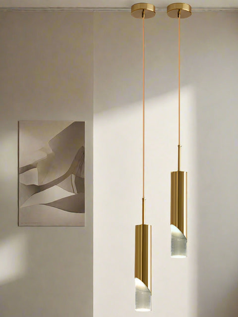 Tatva Lights Cylino Pendant Light – A single elegant gold pendant light with a slim cylindrical body and frosted glass ends, suspended from a minimal ceiling mount. Perfect for adding a modern, luxurious touch to living rooms, dining areas, or bedside corners.
