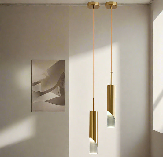 Tatva Lights Cylino Pendant Light – A single elegant gold pendant light with a slim cylindrical body and frosted glass ends, suspended from a minimal ceiling mount. Perfect for adding a modern, luxurious touch to living rooms, dining areas, or bedside corners.
