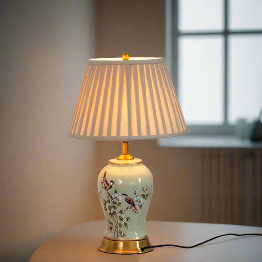 Tatva Lights Floral Ceramic Yellow and Green Table Lamp featuring a hand-painted floral and bird motif on a glazed ceramic base, complemented by a pleated fabric shade and golden accents for a classic and elegant look.