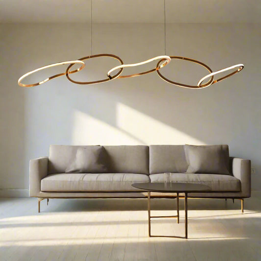 Tatva Lights Contemporary gold LED chandelier with flowing, interconnected oval loops and sculptural wave design, suspended from the ceiling. Statement pendant lighting ideal for modern living rooms, dining areas, or luxury interiors.