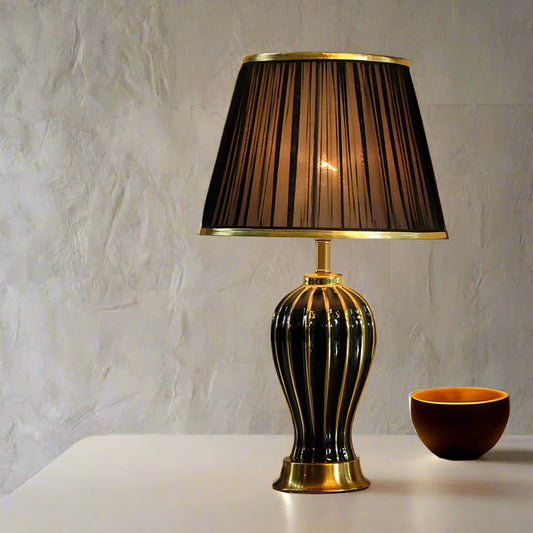 Tatva Lights Golden Accent Ceramic Table Lamp featuring a sleek black ceramic base with vertical gold accents and a matching black pleated lampshade with gold trim—an elegant lighting piece that adds warmth and luxury to any setting.