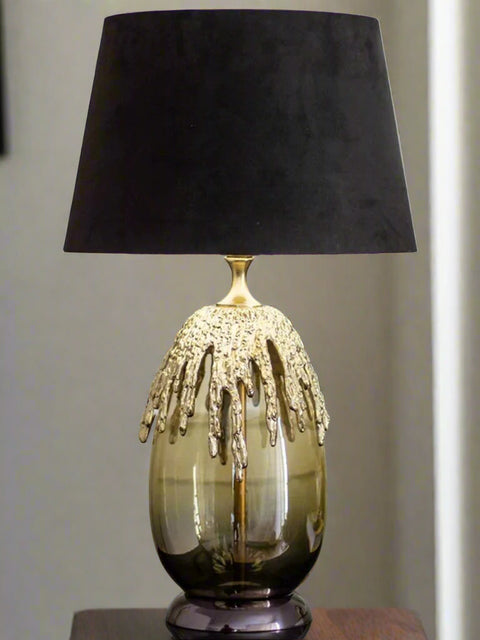 Tatva Lights Lava Luxe Black & Gold Table Lamp featuring a glossy smoked glass base adorned with a dramatic molten gold texture, topped with a bold black velvet lampshade—an artistic and luxurious statement piece for modern interiors.