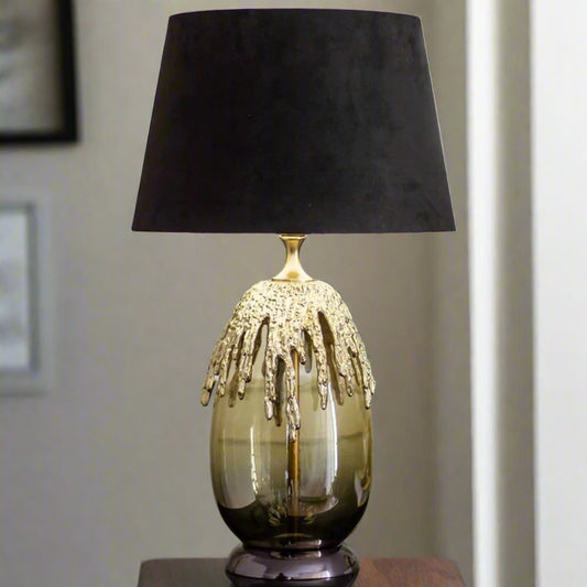 Tatva Lights Lava Luxe Black & Gold Table Lamp featuring a glossy smoked glass base adorned with a dramatic molten gold texture, topped with a bold black velvet lampshade—an artistic and luxurious statement piece for modern interiors.