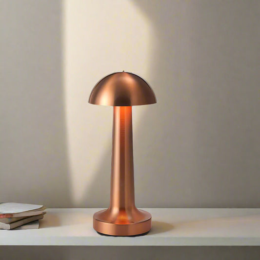 Tatva Lights Mushroom Touch-Control Wireless Bar Table Lamp in a sleek metallic copper finish, featuring a dome-shaped top and slender stem design. Placed on a marble surface against a dark backdrop, the lamp adds a warm, modern glow ideal for contemporary bar or side table settings.