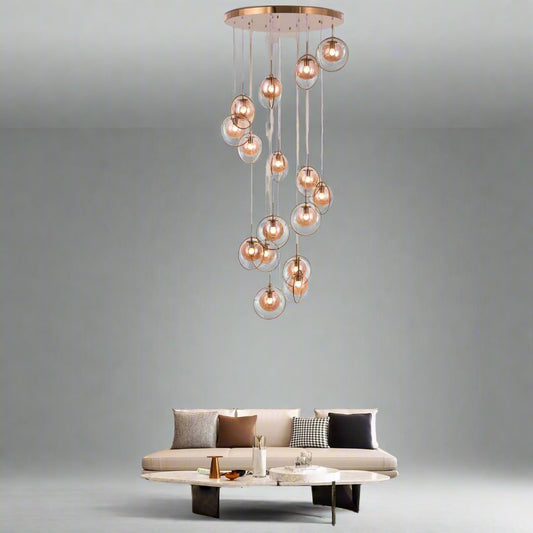 Tatva Lights Novaré Double Height Chandelier features a grand, multi-tiered design with cascading crystal elements and a warm gold finish, ideal for illuminating large foyers, staircases, or double-height living areas with timeless elegance.