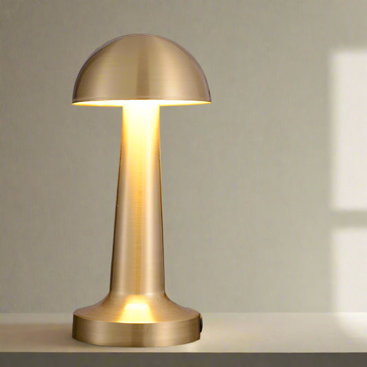 Tatva Lights brushed gold mushroom-style LED table lamp with a sleek dome-shaped head and cylindrical base, placed on a dark marble surface. Ideal for modern dining tables, sideboards, or ambient accent lighting in contemporary interiors