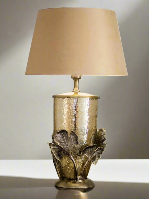 Tatva Lights Tropical Palm Metal Glass Table Lamp featuring a hammered golden glass base with ornate palm leaf metal detailing and a classic beige lampshade, perfect for luxurious vintage or tropical-themed interiors.
