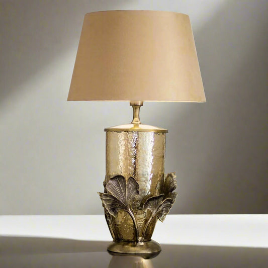 Tatva Lights Tropical Palm Metal Glass Table Lamp featuring a hammered golden glass base with ornate palm leaf metal detailing and a classic beige lampshade, perfect for luxurious vintage or tropical-themed interiors.